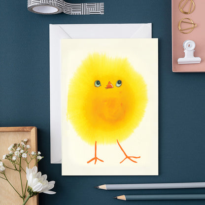 Greeting card with a yellow chick illustration on a blue surface with stationery items.