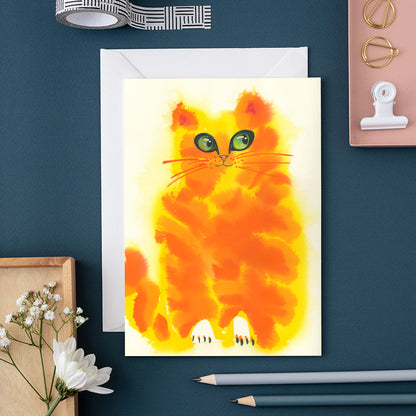 Greeting card with a colorful cat illustration on a blue surface with stationery items.
