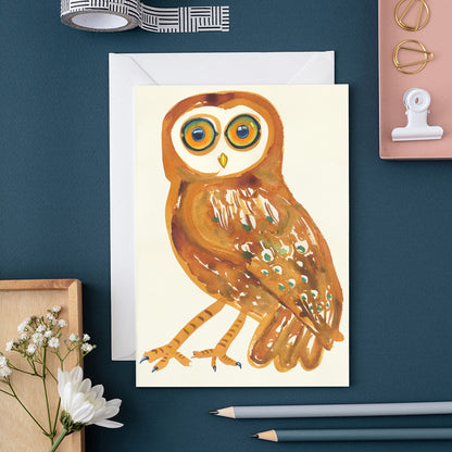 Greeting card with an Tawny owl design on a blue surface with stationery items.