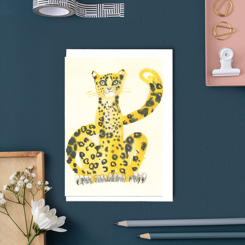 Greetings card Yellow cheetah on a white background, displayed on a blue desk with decorative items.
