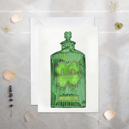 Green glass bottle with a shamrock design and 'Luck' text on a white card, set against a light gray background.